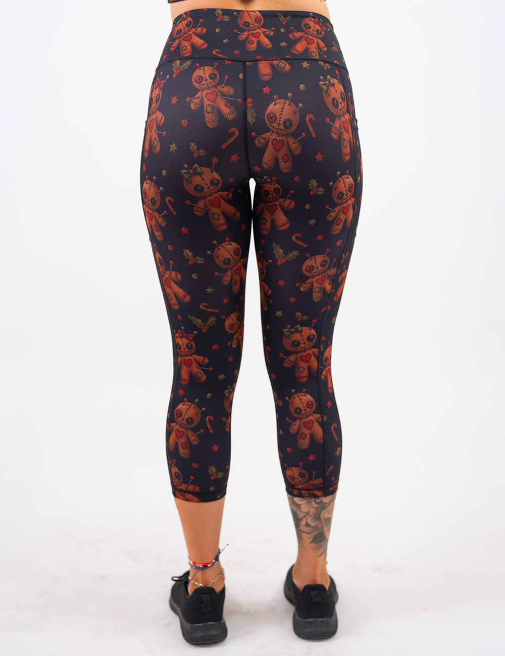 back of the gingerbread voodoo dolls with pins in them surrounded by berries and stars on a black background capri leggings