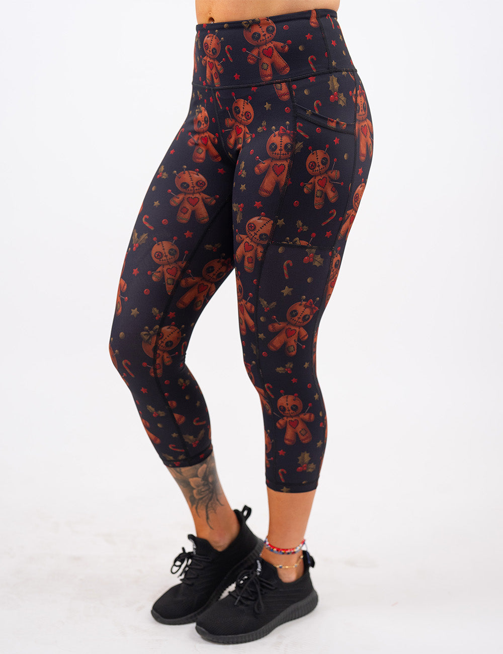 front of the gingerbread voodoo dolls with pins in them surrounded by berries and stars on a black background capri leggings