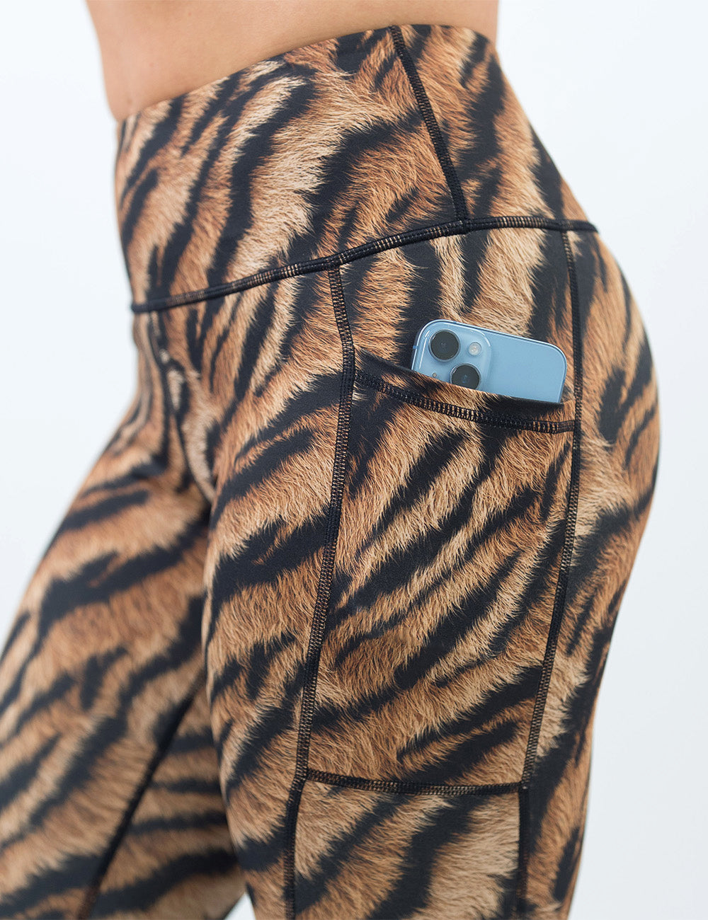 close up of the tiger print leggings with a phone in it pocket against a white background