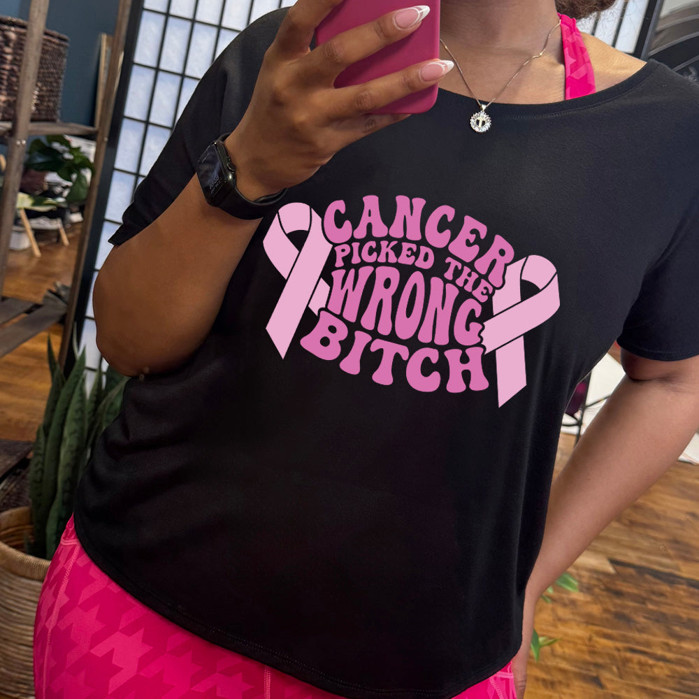 Person wearing a black t-shirt with pink text that says "Cancer Picked The Wrong Bitch" and a pink ribbon design on it