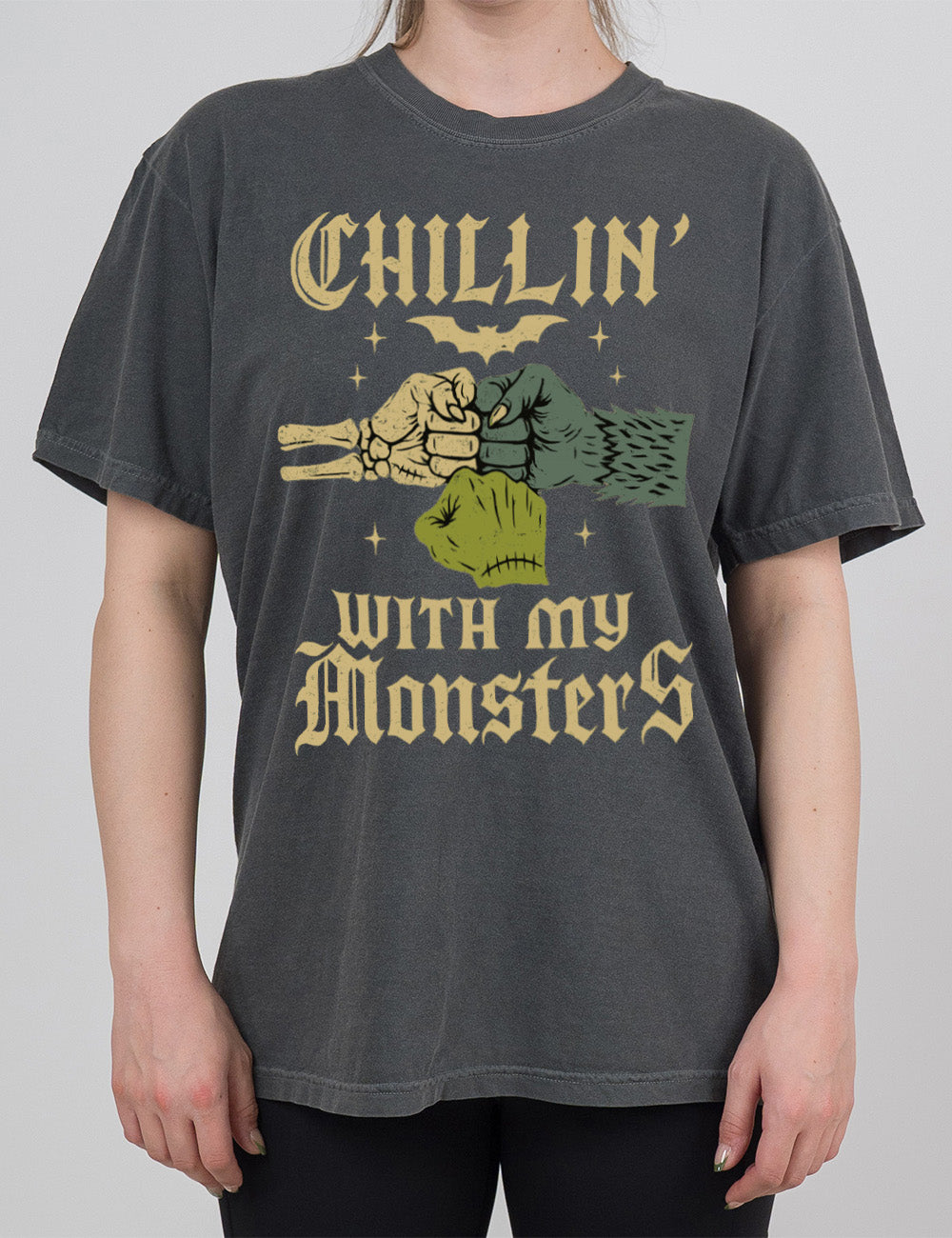 pepper modern tee with the words "chillin' with my monsters" around the graphic of a skeleton's hand, a werewolf's hand, and a zombie's hand, doing a fist pump, with a bat above, and few stars around