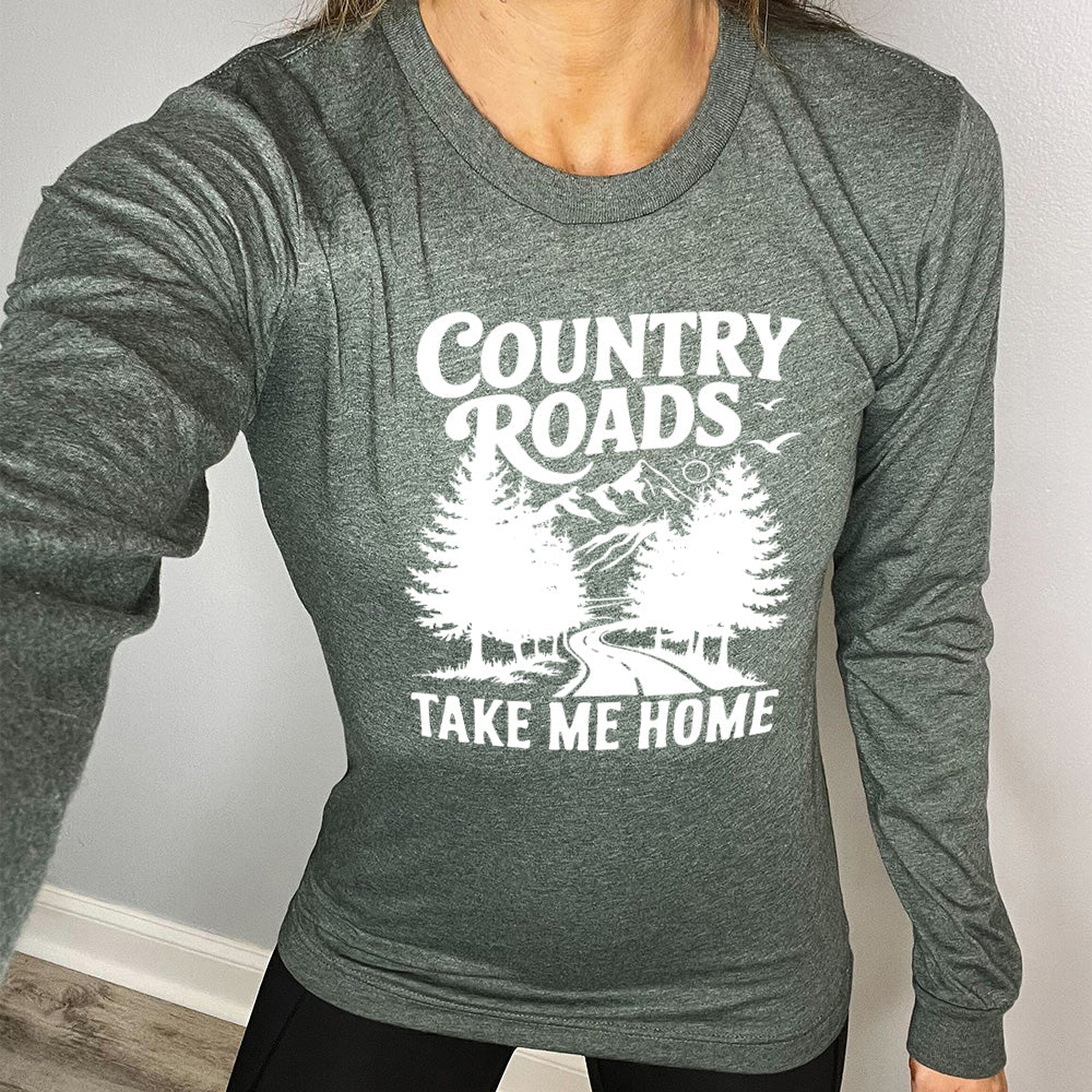 heather forest long sleeve with the words "country roads take me home" on it, and the graphic of a road going through tall trees, with mountains beyond, and the sun