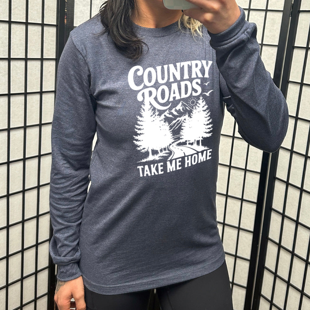heather navy long sleeve with the words "country roads take me home" on it, and the graphic of a road going through tall trees, with mountains beyond, and the sun