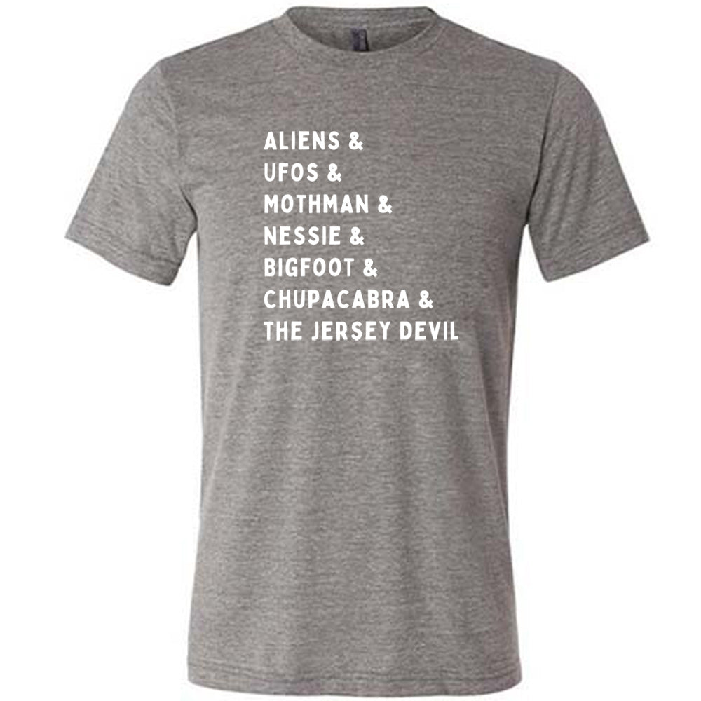 Grey colored shirt with graphic on it that says "ALIENS & UFOS & MOTHMAN & NESSIE & BIGFOOT & CHUPACABRA & THE JERSEY DEVIL"