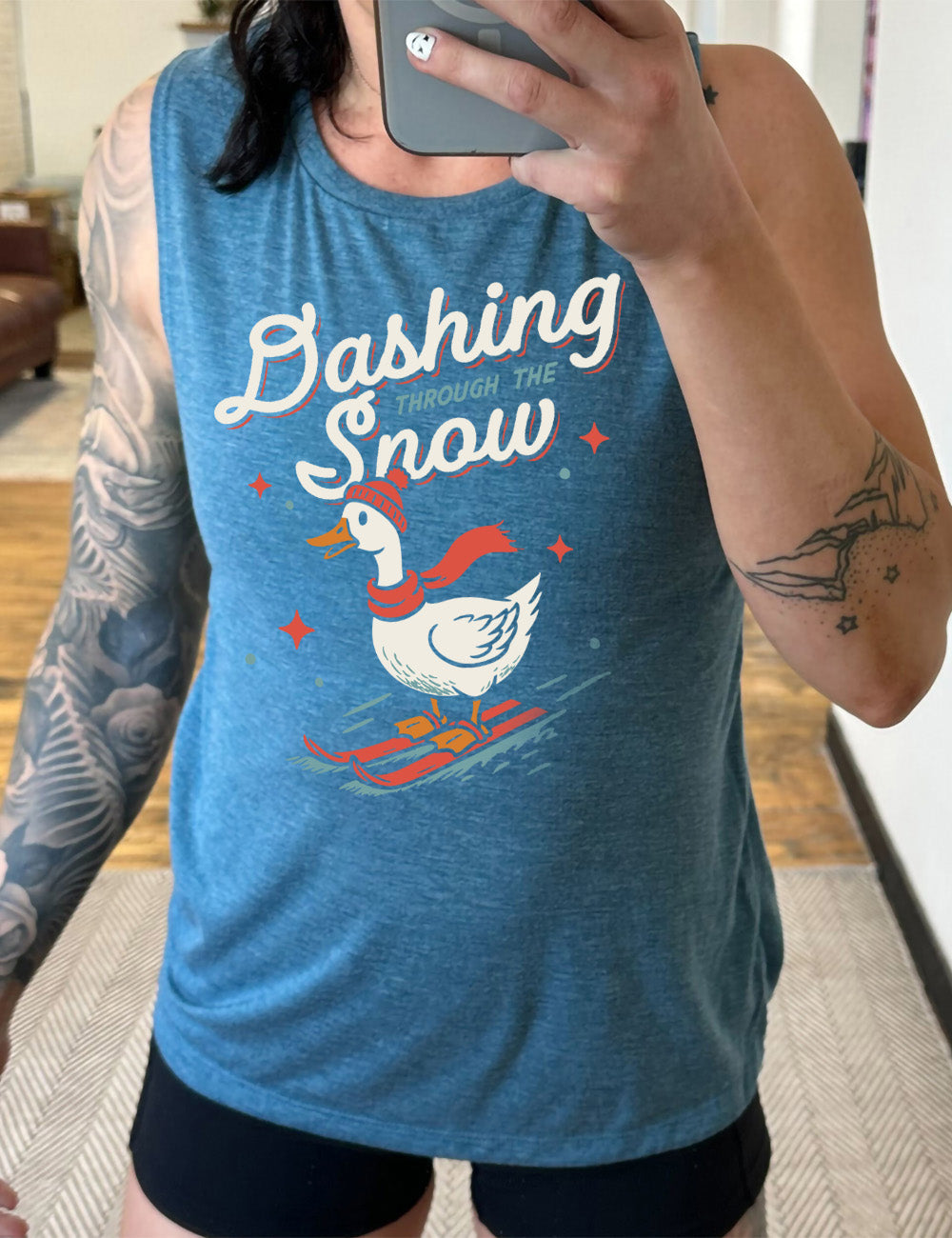deep teal muscle tank with the graphic of a goose, wearing a hat and scarf, on skis, in downwards motion, with some stars, and the words above it saying "Dashing through the Snow"