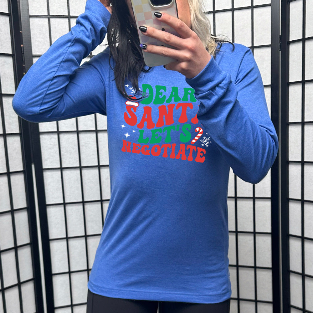 heather royal blue long sleeve with the words "dear santa let's negotiate" with some snowflakes, stars, and a candy cane