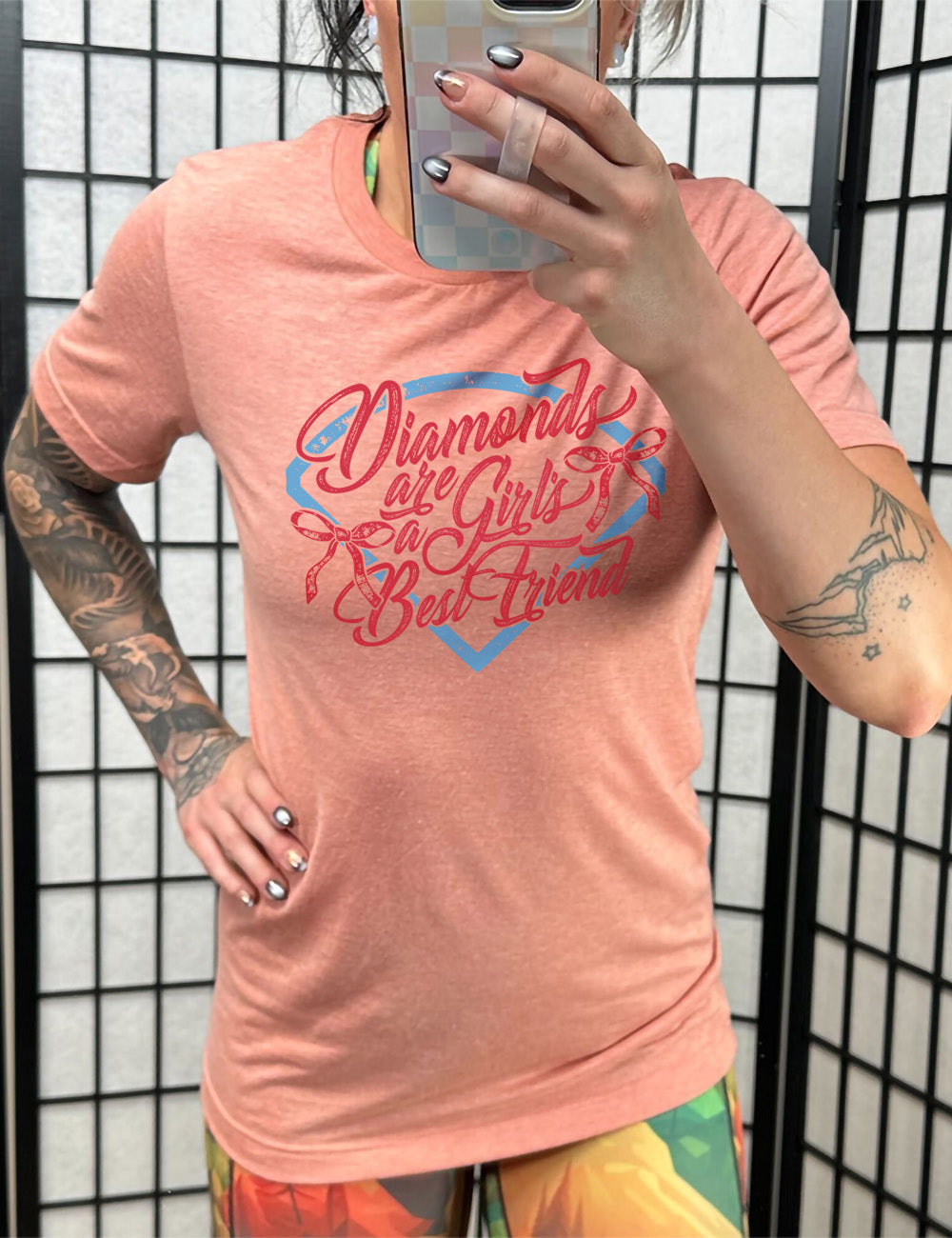 sunset unisex tee with the words "diamonds are a girl's best friend" on it, with two bows, all in front of a baseball diamond