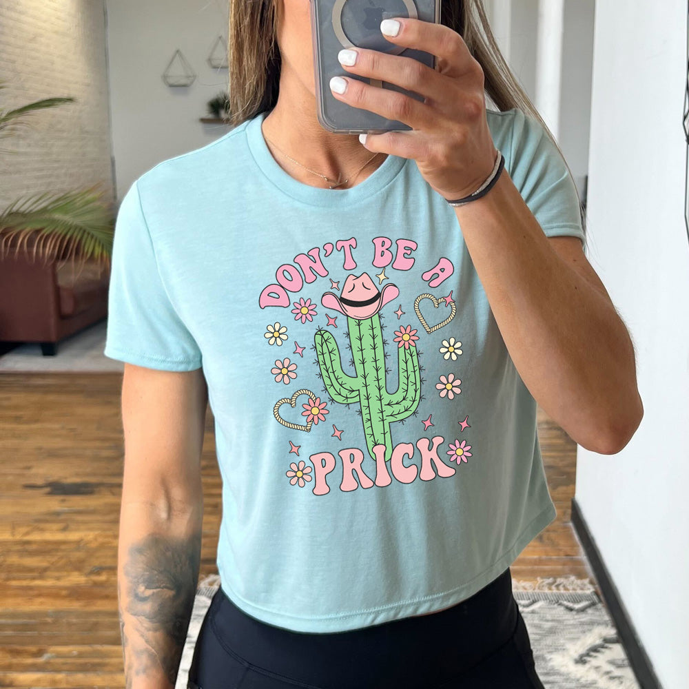 dusty blue cropped tee with a cactus wearing a cowboy hat graphic on it that says "Don't Be A Prick"