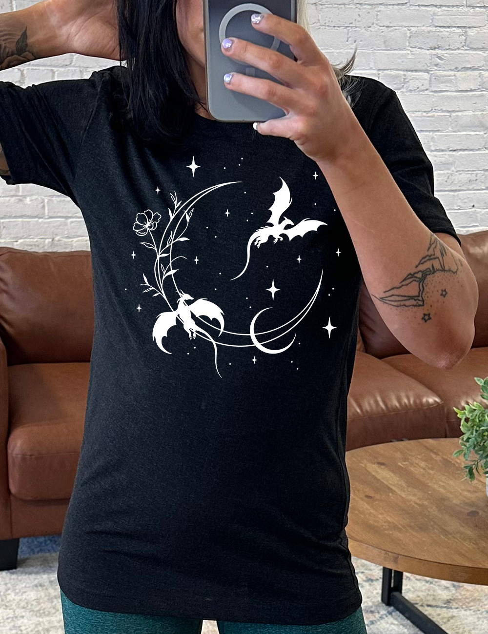 black unisex tee with the graphic of a large crescent moon, with a flower lining it, two dragons flying, another smaller moon, and many small stars