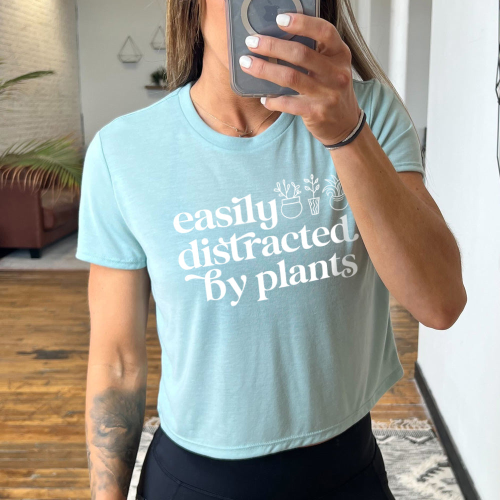 Model wearing dusty blue colored cropped top with a potted plant graphic on it that says "Easily Distracted By Plants"