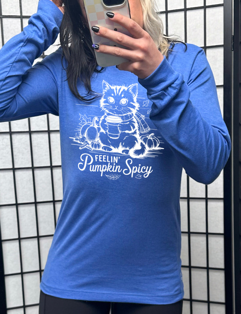 heather true royal long sleeve with the graphic of a cat, wearing a scarf, next to a few pumpkins of various sizes and a few falling leaves, holding a takeaway coffee, and the words underneath saying "feelin' pumpkin spicy"