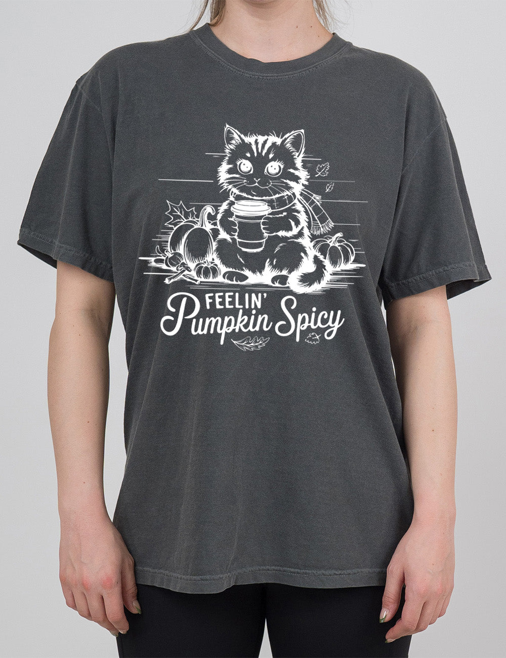 pepper modern tee with the graphic of a cat, wearing a scarf, next to a few pumpkins of various sizes and a few falling leaves, holding a takeaway coffee, and the words underneath saying "feelin' pumpkin spicy"