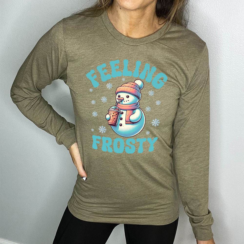 heather olive long sleeve shirt with the words "feeling frosty" on it, with the graphic of snowperson, wearing a hat and scarf, drinking an iced drink, surrounded by snowflakes