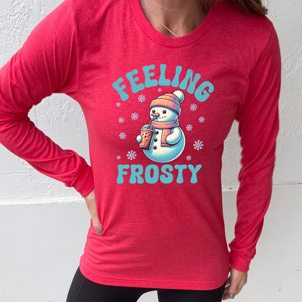 heather red long sleeve shirt with the words "feeling frosty" on it, with the graphic of snowperson, wearing a hat and scarf, drinking an iced drink, surrounded by snowflakes