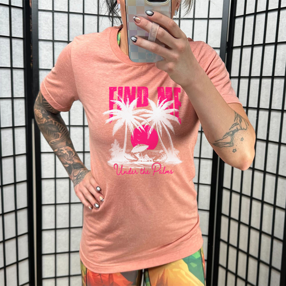 Model wearing sunset colored shirt with a beach and palm trees graphic on it that says "Find Me Under The Palms"