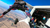 Person skydiving from an airplane with a clear blue sky and landscape below.