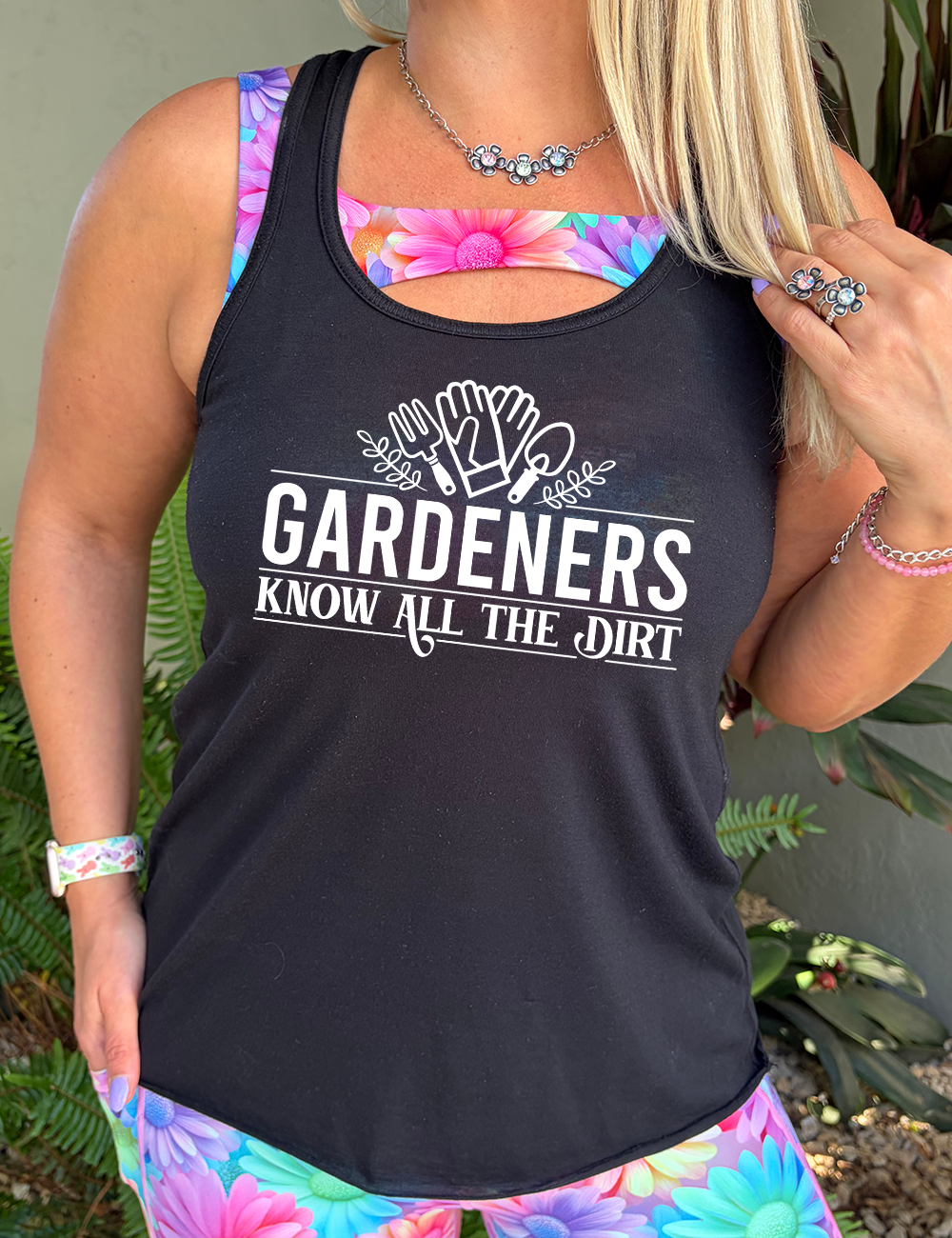 black flowy racerback tank with the words "gardeners know all the dirt" on it, with the graphic of two gloves and two tools above the words