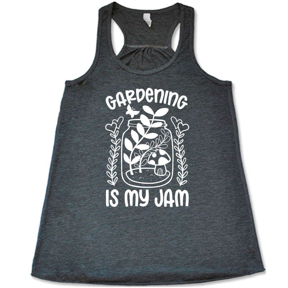 grey flowy racerback tank with the words "gardening is my jam" on it, and the graphic of a jar with plants and a mushroom in it, a little butterfly flying above it, and a plant (with hearts for flowers on them) on both sides of it