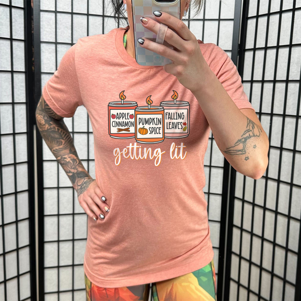 Model wearing sunset colored shirt with fall scented candles graphic on it that says "getting lit"