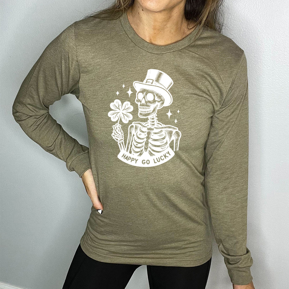 heather olive long sleeve shirt with the graphic of a skeleton wearing a leprechaun hat and holding a four-leaf clover, with a few little stars around, and the text "happy go lucky" underneath
