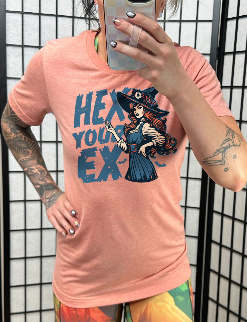 sunset unisex tee with the words "hex your ex" on it, next to the detailed, colorful graphic of a long-haired witch, hand on hip, other hand raised, wearing a flowery witch hat, and an old-fashioned dress