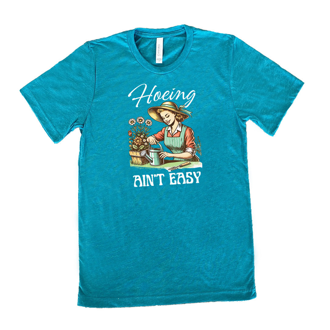 Teal colored shirt with a woman gardening graphic on it that says "Hoeing Ain't Easy"