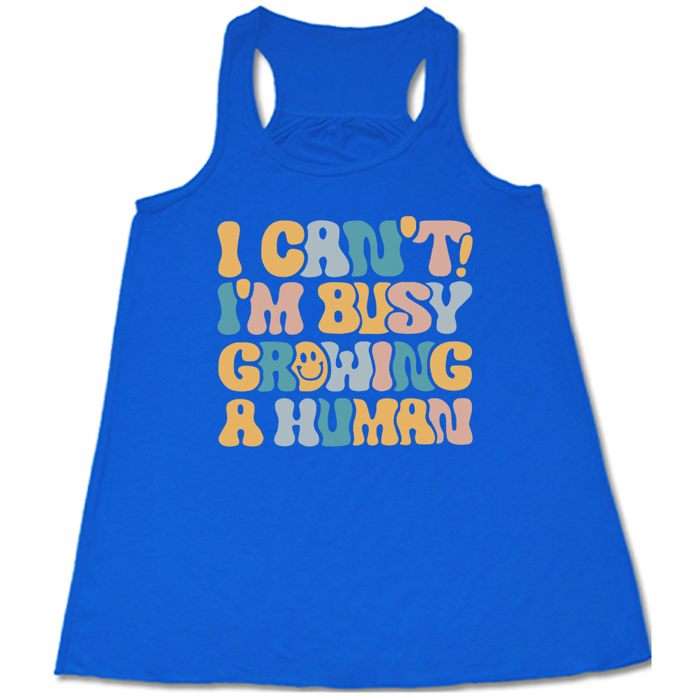 blue racerback flowy tank with the words "I can't! I'm busy growing a human" on it in colorful font, with a smiley face in the "o" of the word "growing"