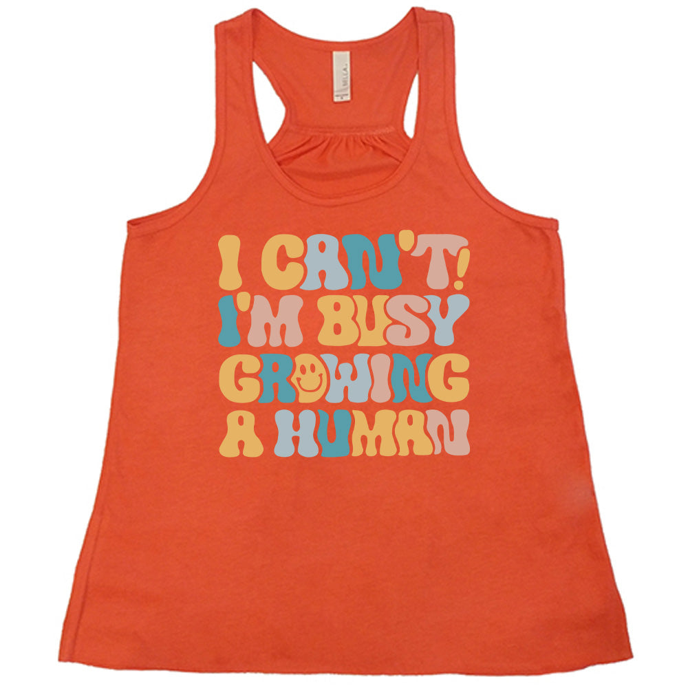 coral racerback flowy tank with the words "I can't! I'm busy growing a human" on it in colorful font, with a smiley face in the "o" of the word "growing"