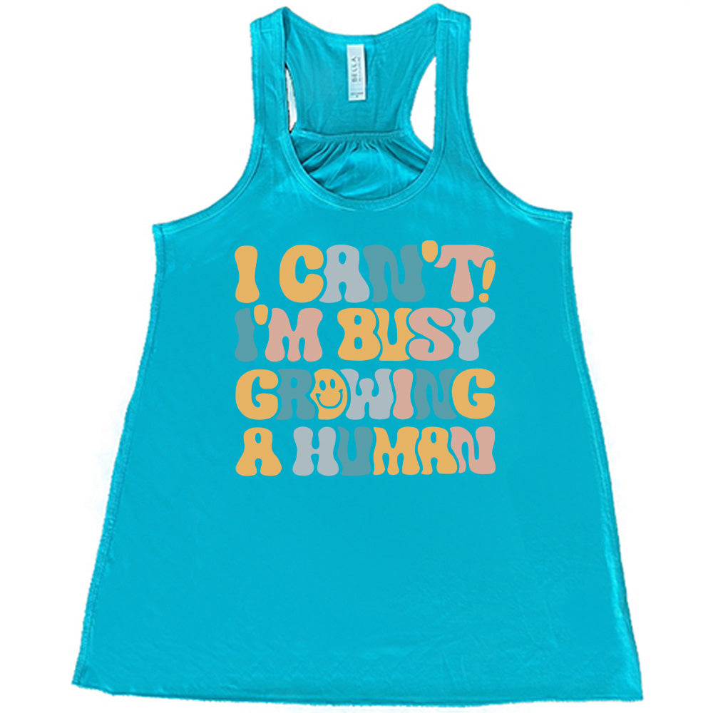 teal racerback flowy tank with the words "I can't! I'm busy growing a human" on it in colorful font, with a smiley face in the "o" of the word "growing"