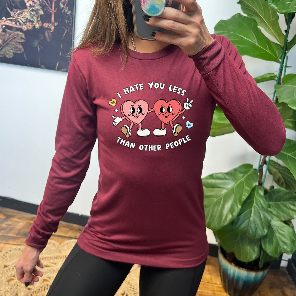 heather cardinal long sleeve shirt with the text "I Hate You Less Than Other People" on it, and the graphics of two heart people, arms on each other, smiling