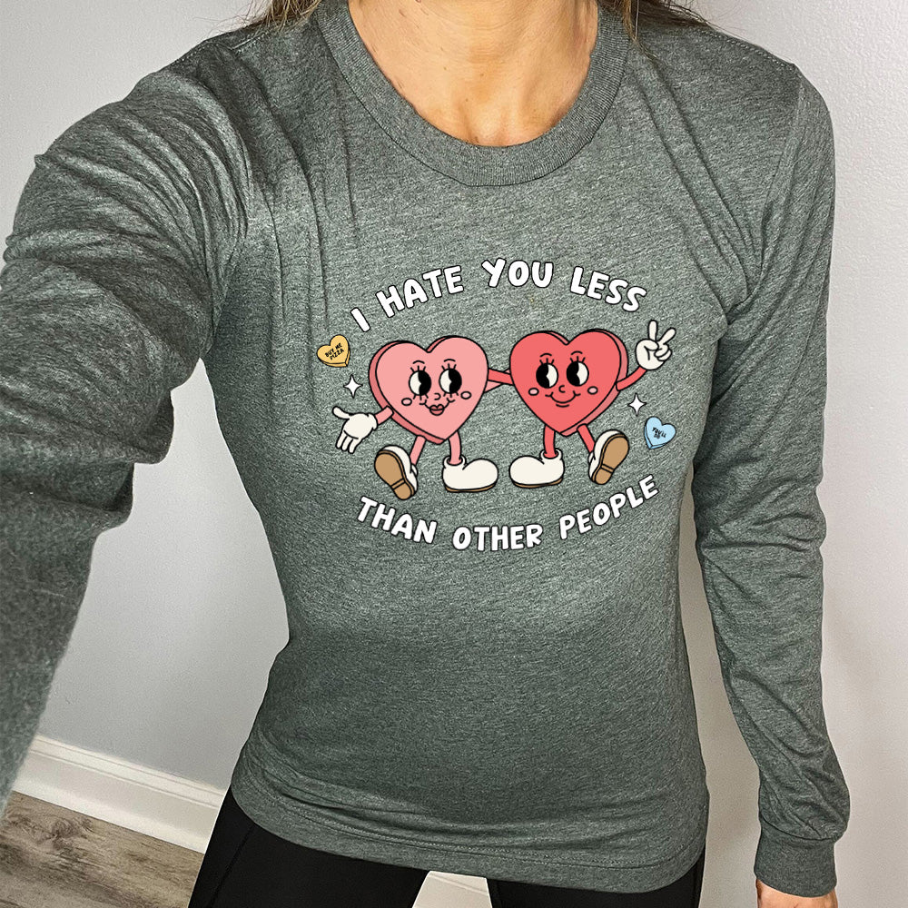heather forest long sleeve shirt with the text "I Hate You Less Than Other People" on it, and the graphics of two heart people, arms on each other, smiling