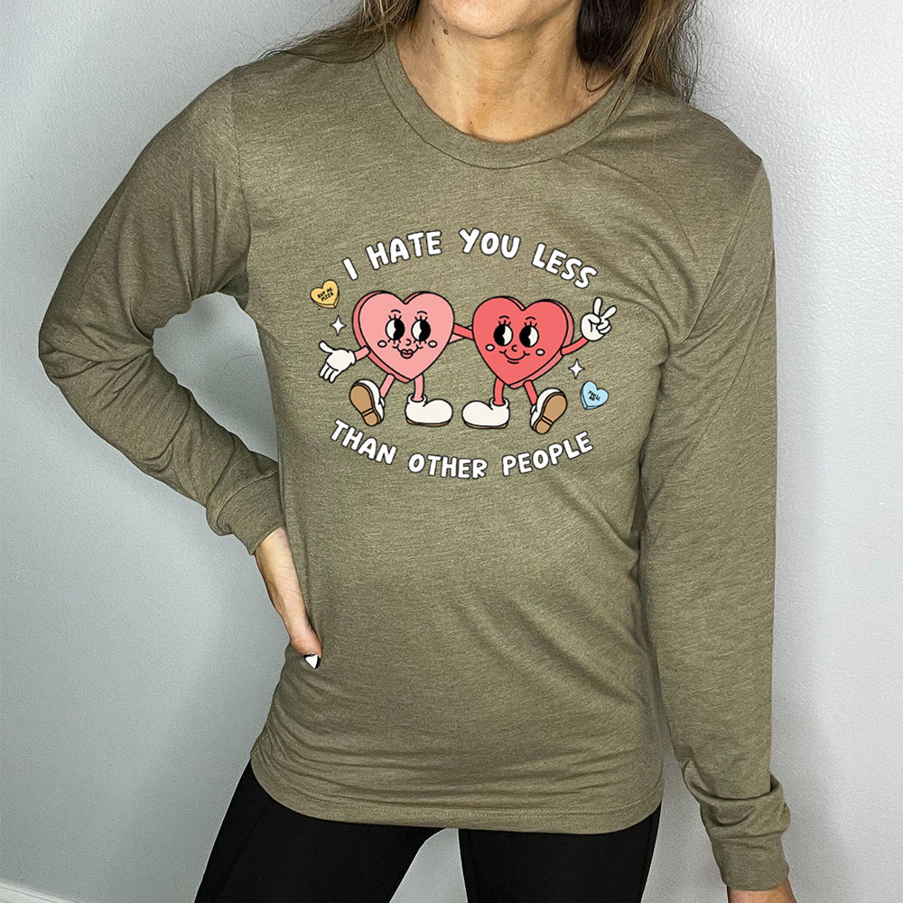 heather olive long sleeve shirt with the text "I Hate You Less Than Other People" on it, and the graphics of two heart people, arms on each other, smiling