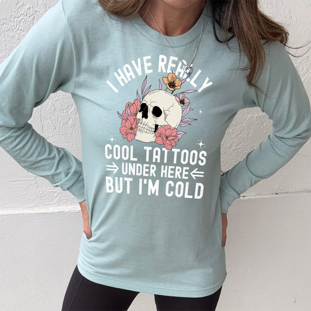 heather dusty blue long sleeve with the words "I have really cool tattoos under here but I'm cold" with the image of a skull in flowers