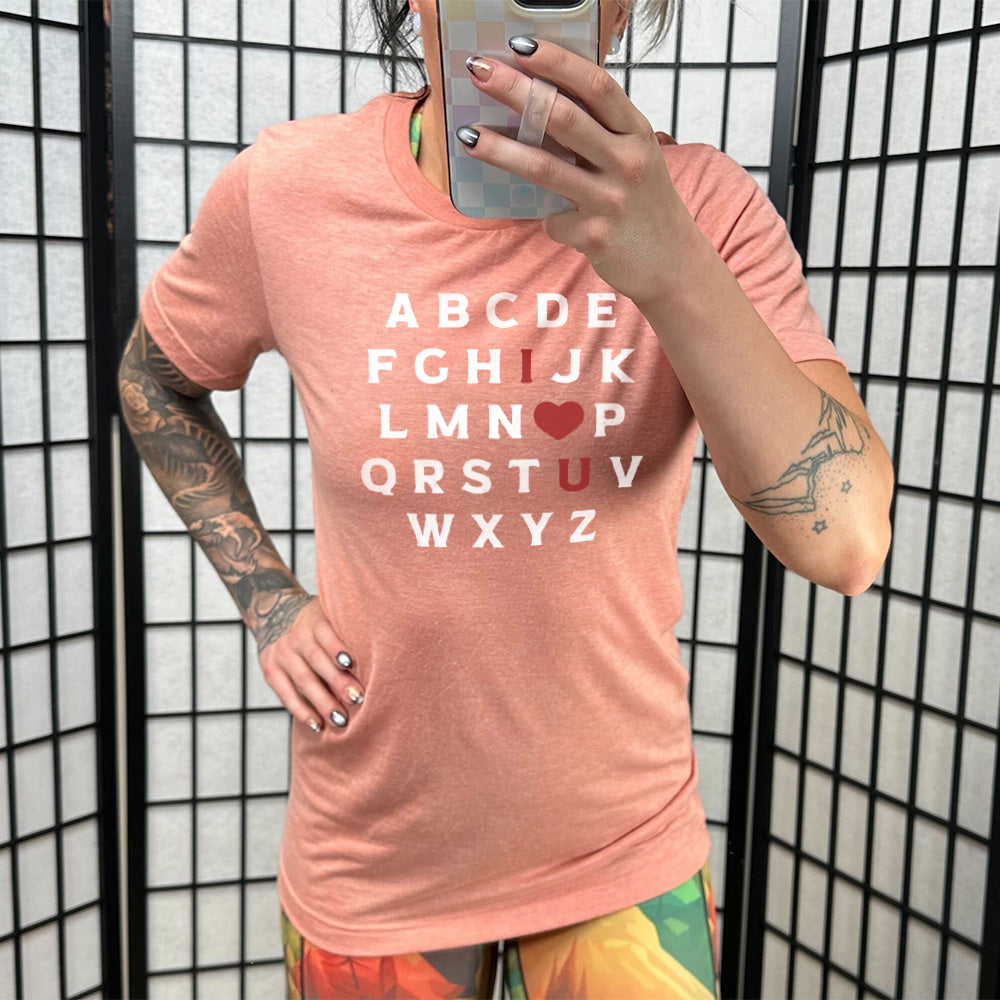 sunset unisex tee with the alphabet on it in white lettering, but with the "I" in red, the "O" turned into a red heart, and "U" in red