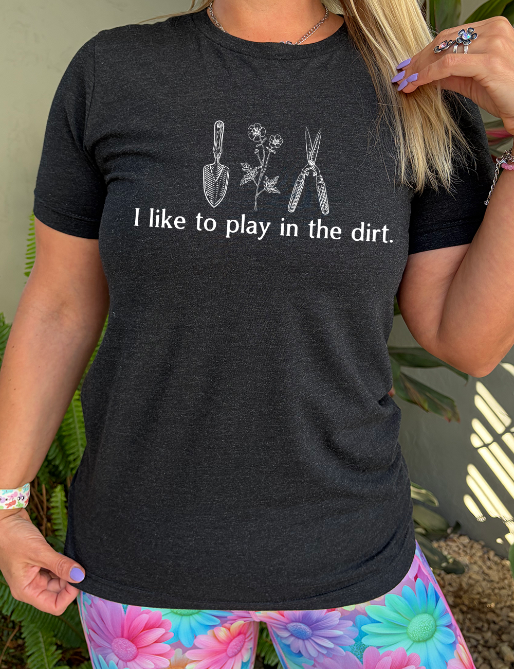 black unisex tee with the words "I like to play in the dirt." on it with the graphic of a hand trowel, two flowers, and shears