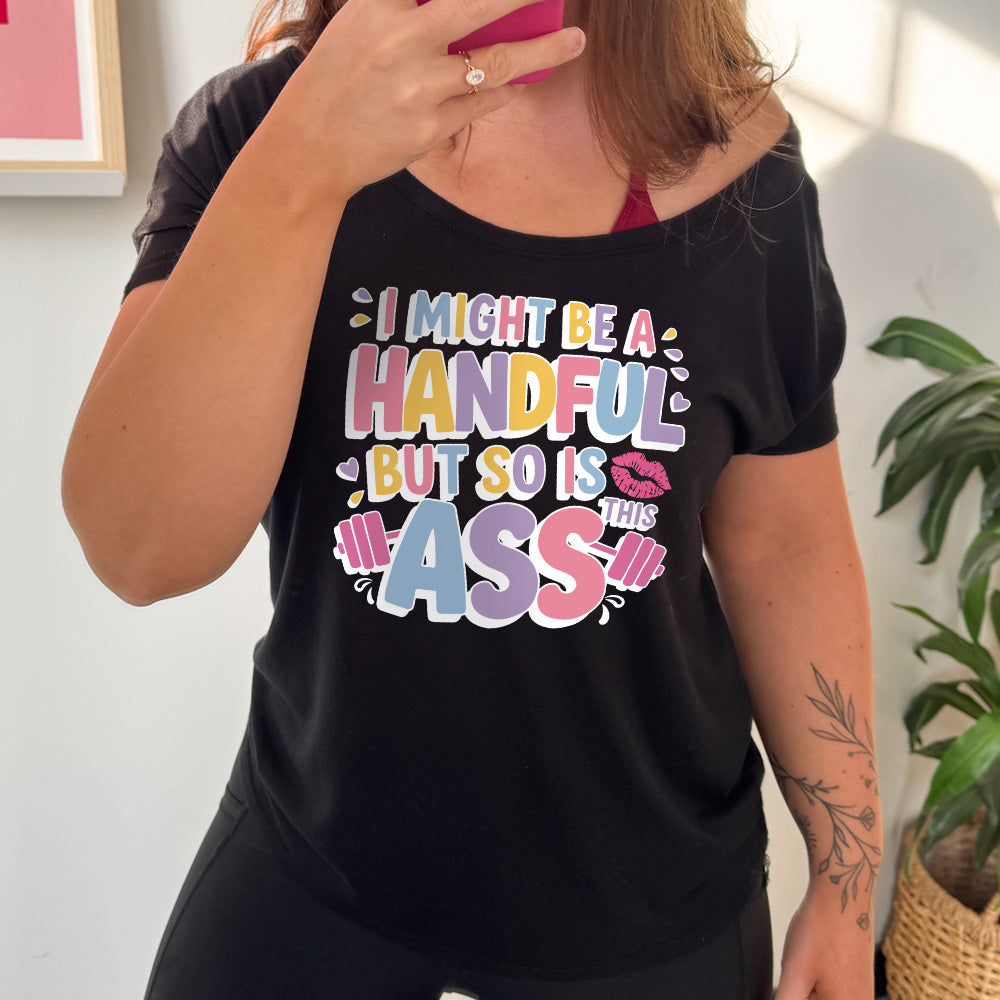 black slouchy tee with the words "I might be a handful but so is this ass" in a colorful font, with a barbell as part of the word "ass", and a few little hearts and a kissing lips graphic