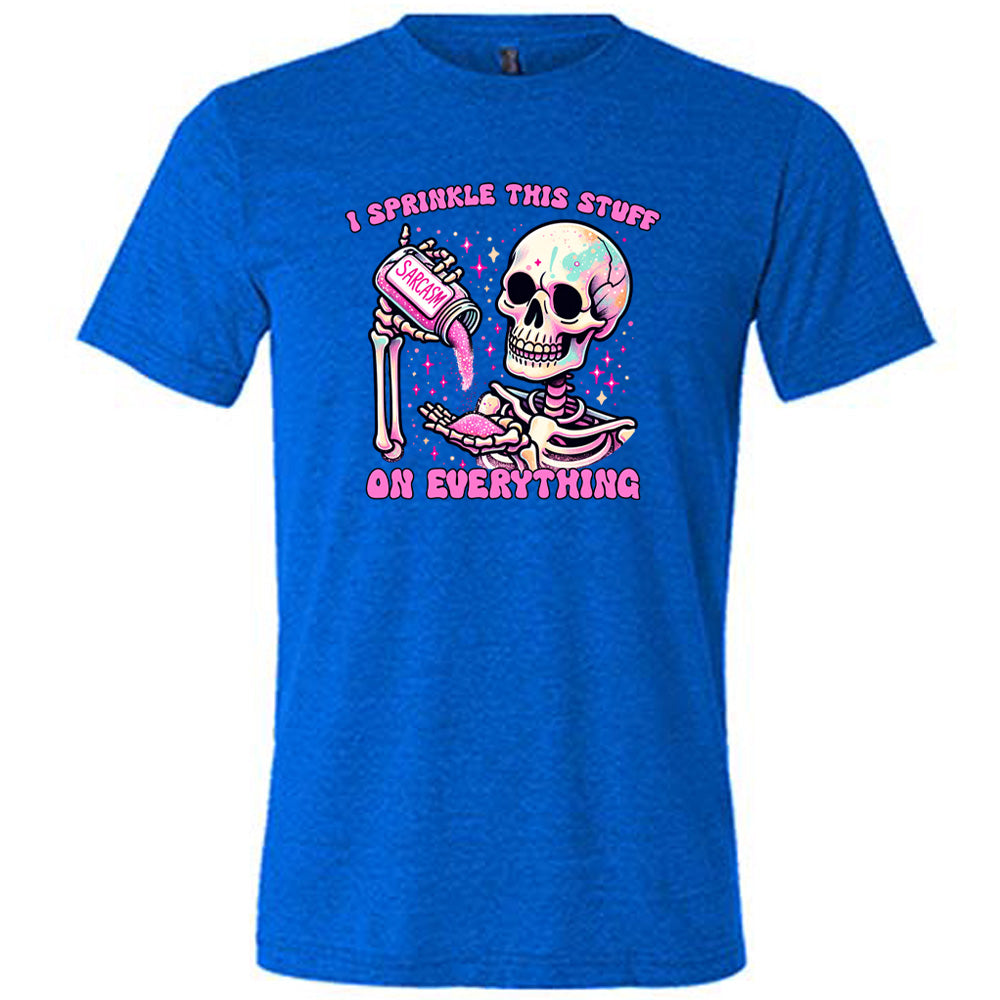 blue unisex tee with the words "I sprinkle this stuff on everything" on it, and the graphic of a skeleton who is pouring a jar labeled "sarcasm" filled with pink glittery material into its hand, surrounded by little pink and white stars