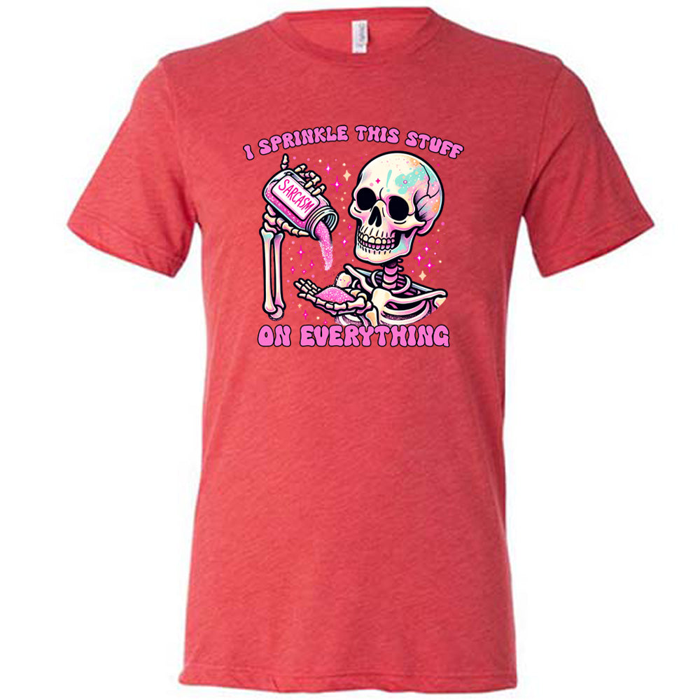 red unisex tee with the words "I sprinkle this stuff on everything" on it, and the graphic of a skeleton who is pouring a jar labeled "sarcasm" filled with pink glittery material into its hand, surrounded by little pink and white stars