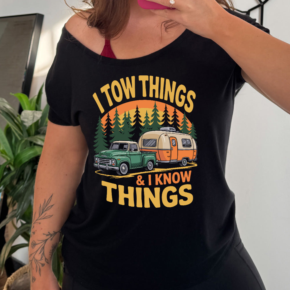 black slouchy tee with the words "I tow things & I know thing" on it, with the graphic of an old-fashioned truck pulling a camper on a road lined with tall trees