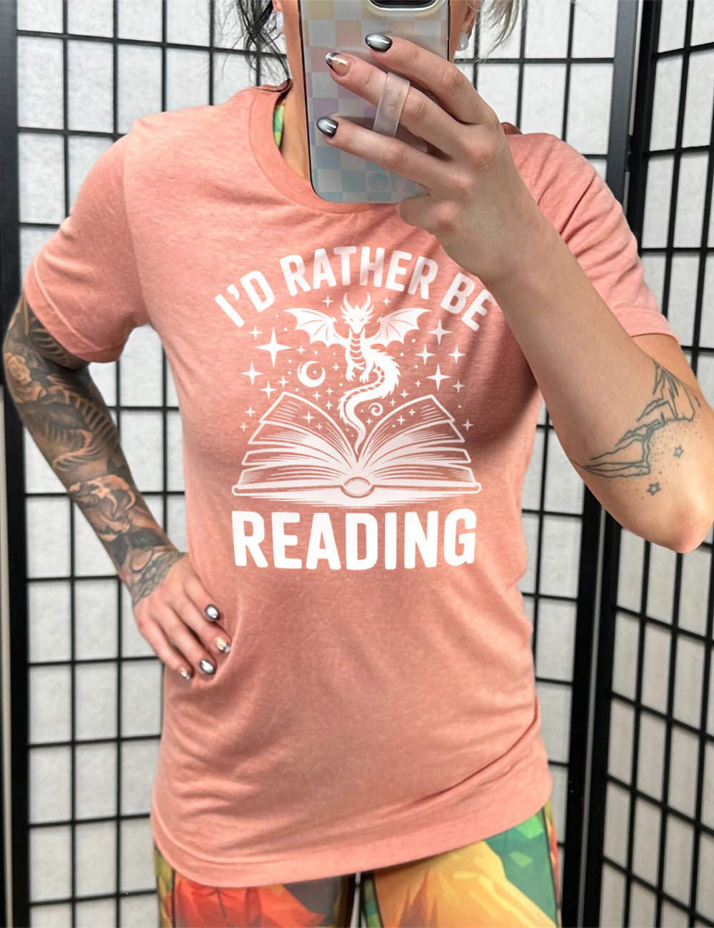 sunset unisex tee with the words "I'd rather be reading" around the graphic of a dragon, hovering out of an open book, with stars all about