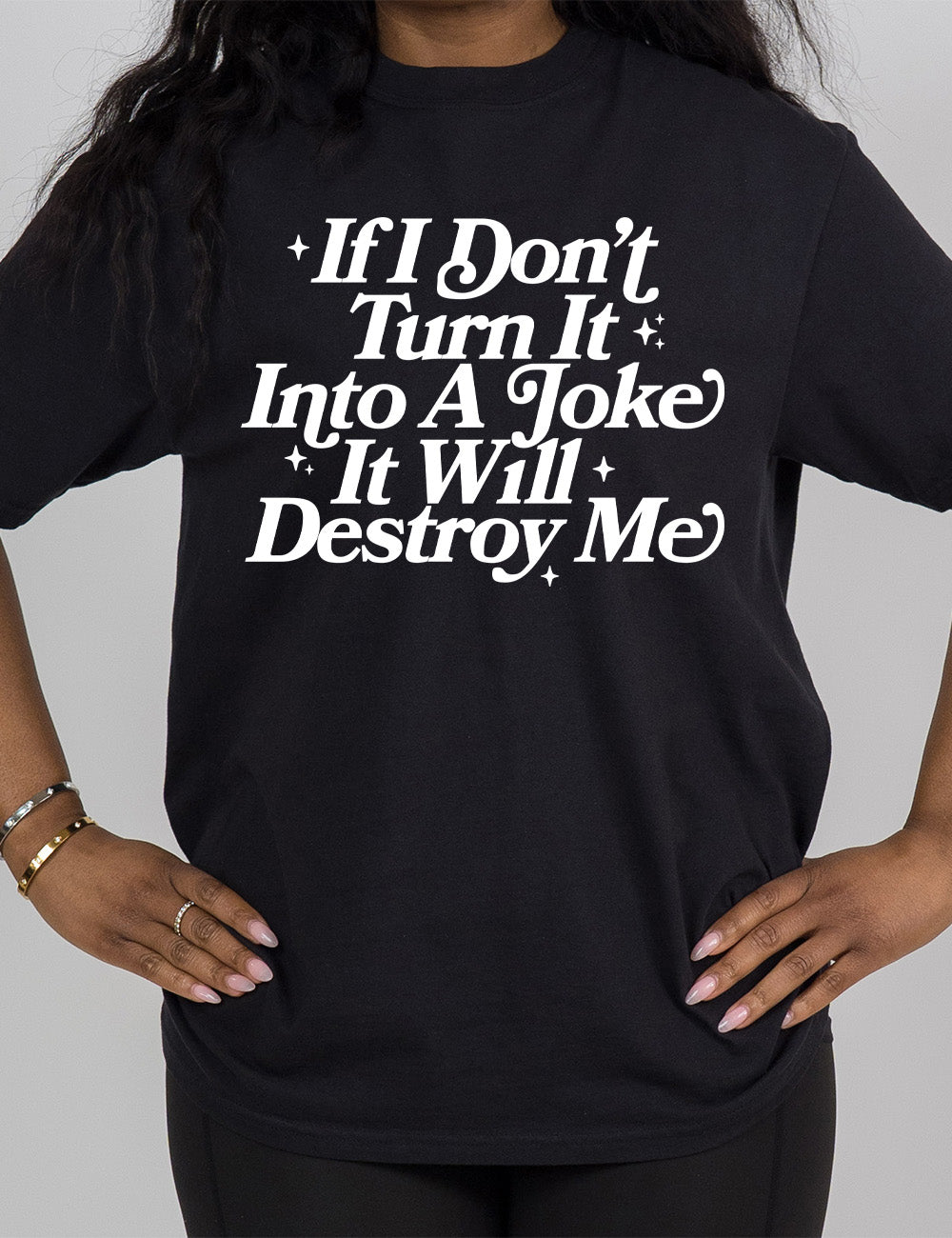black modern tee with words on it saying "If I don't turn it into a joke it will destroy me", embellished by little star graphics