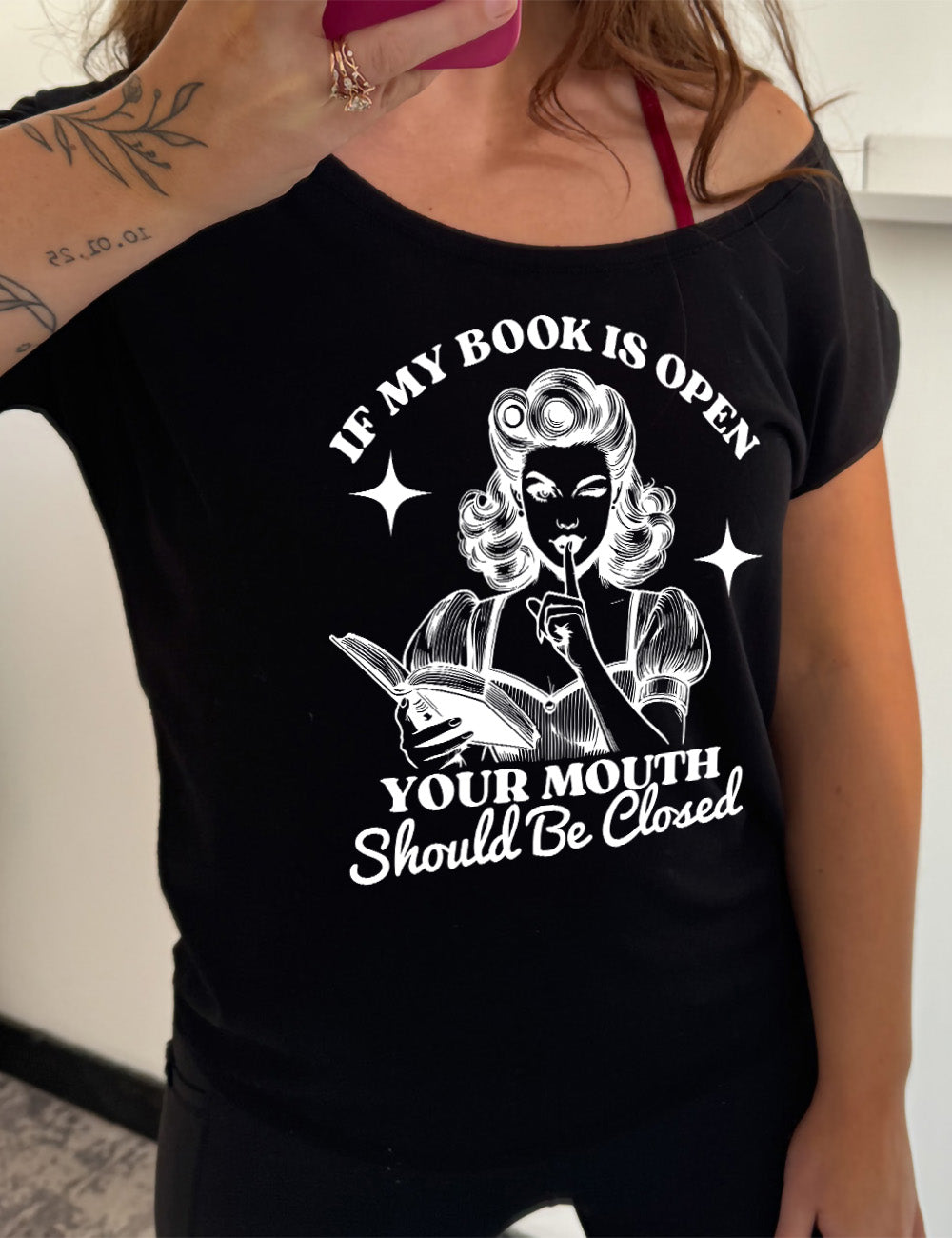 black slouchy tee with the words "If my book is open your mouth should be closed" on it, around the graphic of 950s era woman, holding a finger to her lips, with an open book in her other hand, with a star on either side of her