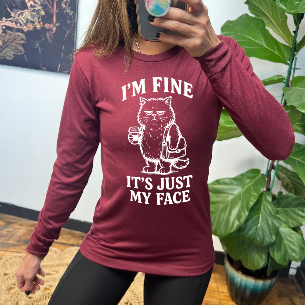 heather cardinal long sleeve shirt with the words "I'm fine it's just my face" on it, around the graphic of a cat with a resting-grumpy face, holding a coffee and wearing a purse
