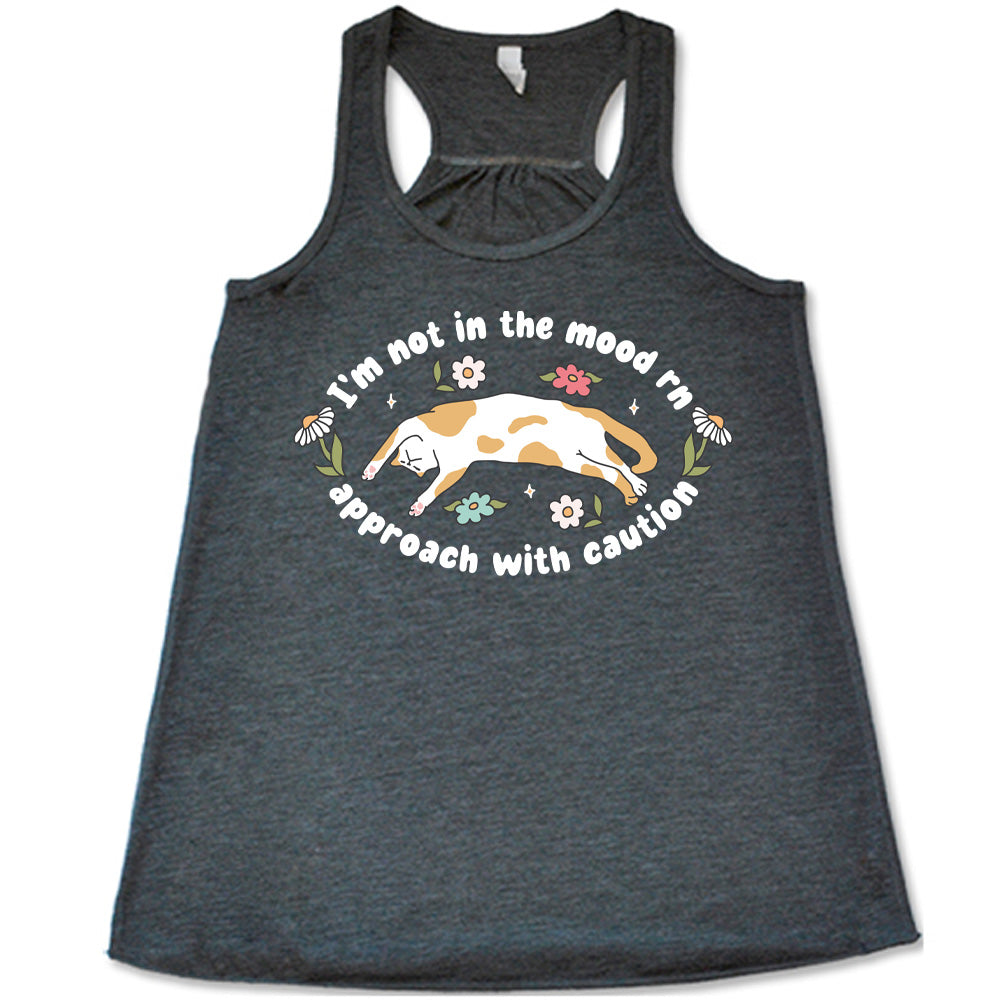 grey racerback tank with the words "I'm not in the mood rn approach with caution" on it in an oval, with the graphic of a cat splayed on its back within the words, and a few flowers around