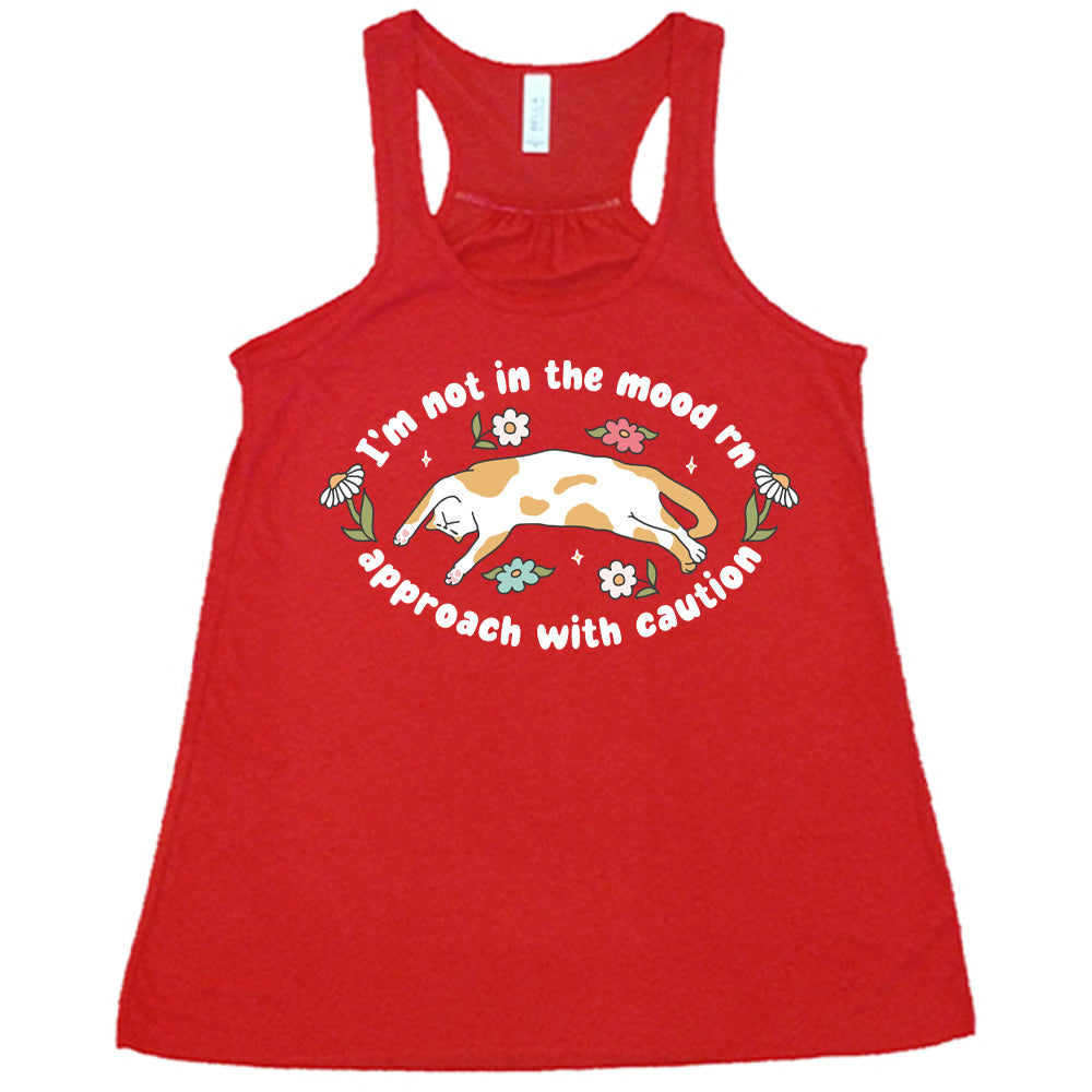 red racerback tank with the words "I'm not in the mood rn approach with caution" on it in an oval, with the graphic of a cat splayed on its back within the words, and a few flowers around