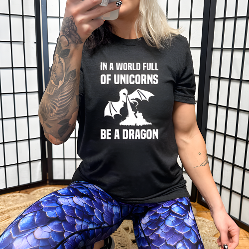 model wearing a black unisex shirt with the saying "In A World Full Of Unicorns Be A Dragon" on it in white