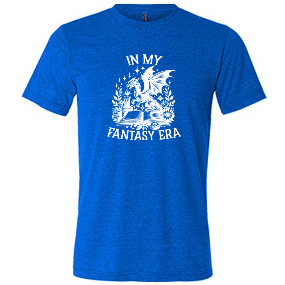 Blue colored shirt with a dragon lighting a candle over a book graphic on it that says "In My Fantasy Era"