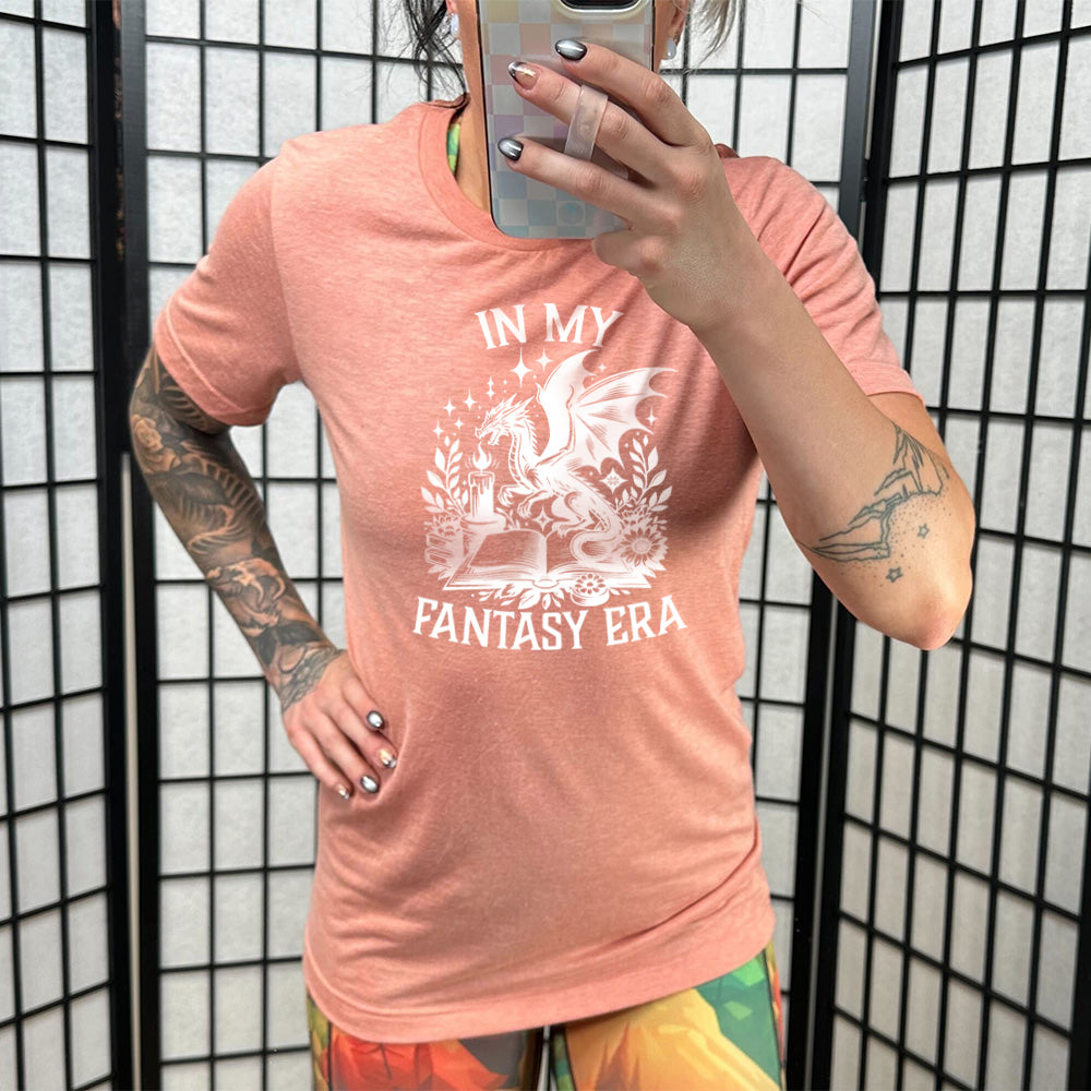 Model wearing sunset colored shirt with a dragon lighting a candle over a book graphic on it that says "In My Fantasy Era"
