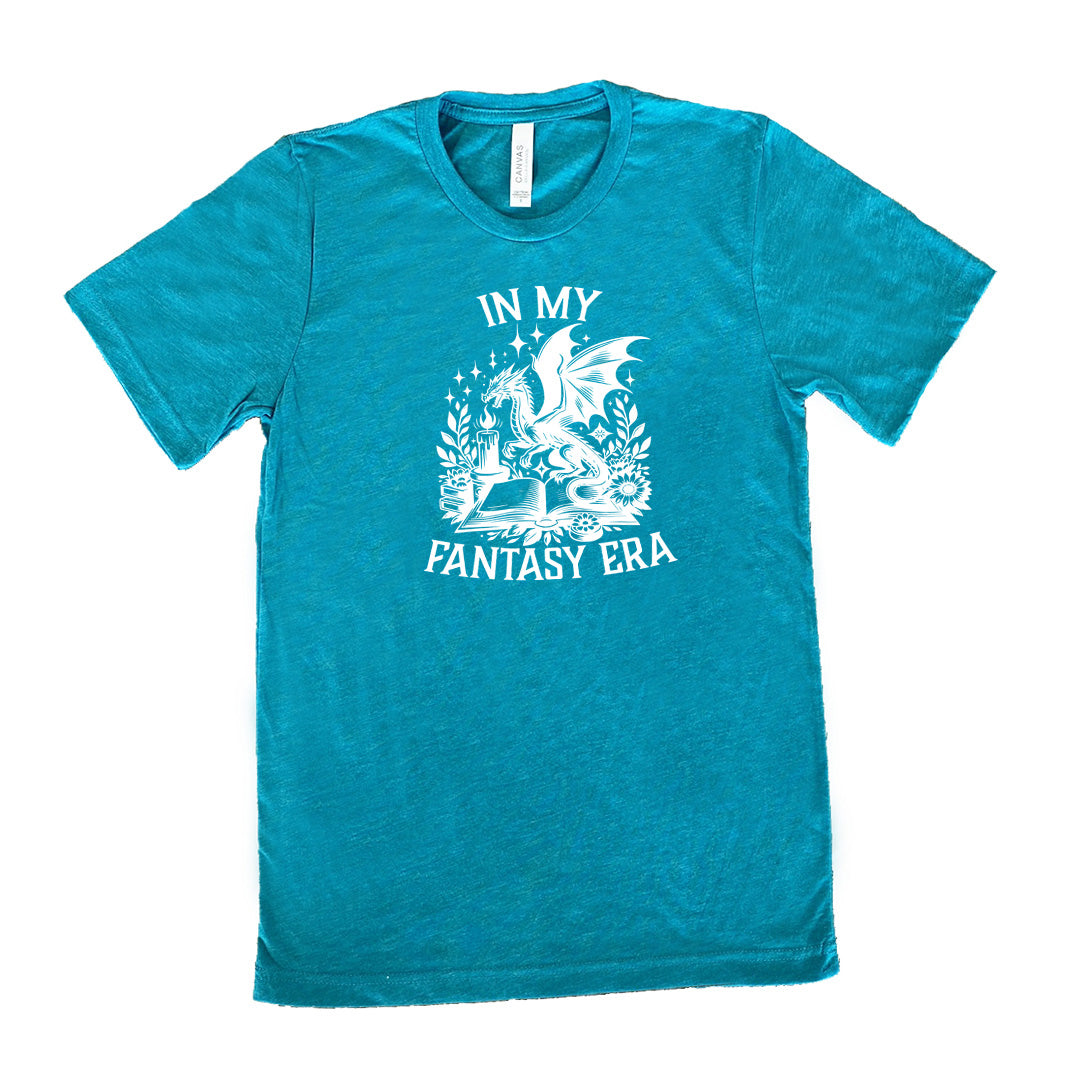 Teal colored shirt with a dragon lighting a candle over a book graphic on it that says "In My Fantasy Era"