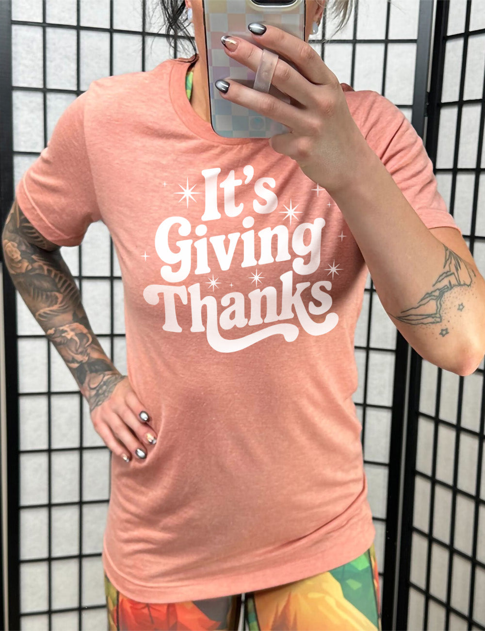 sunset unisex tee with the words "It's Giving Thanks" on it, surrounded by graphics of little stars